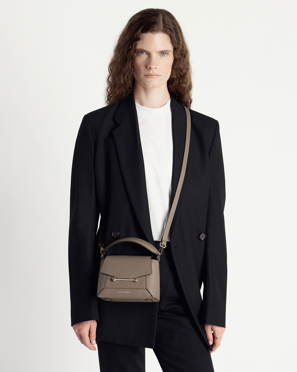 Model wearing taupe Strathberry Mosaic Nano bag with top handle and crossbody strap.