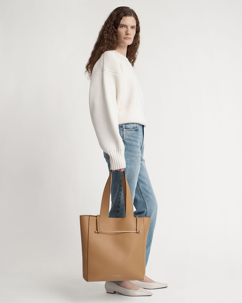 Woman standing in white jumper and jeans holding a caramel tote bag