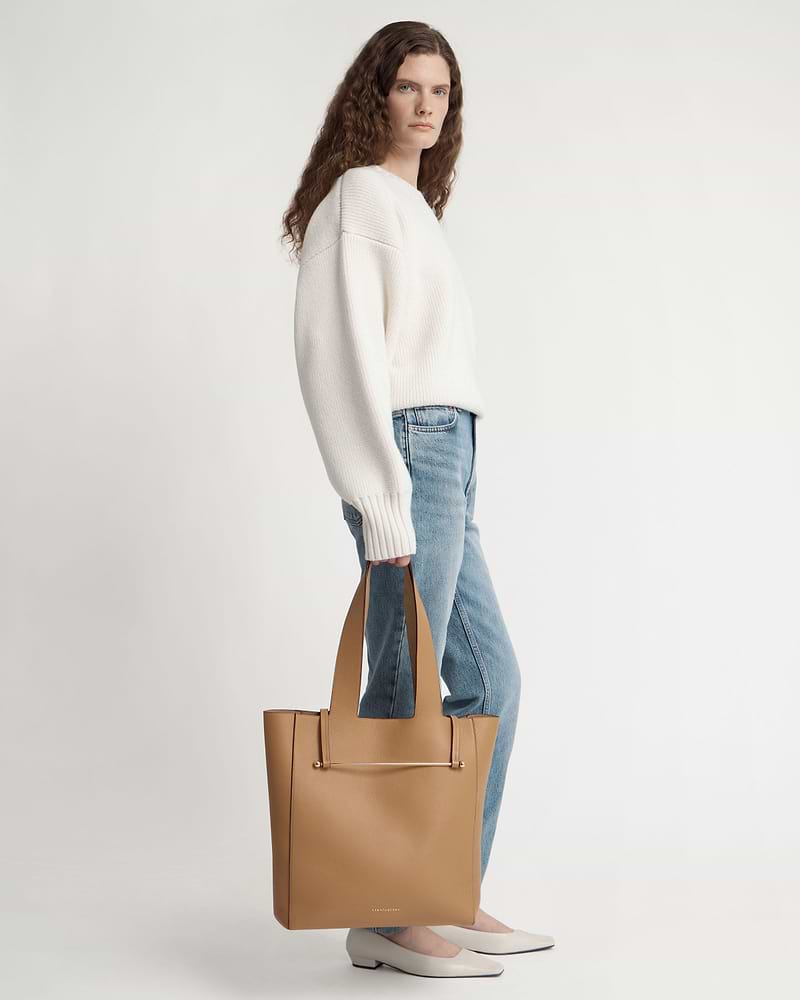 Woman standing in white jumper and jeans holding a caramel tote bag
