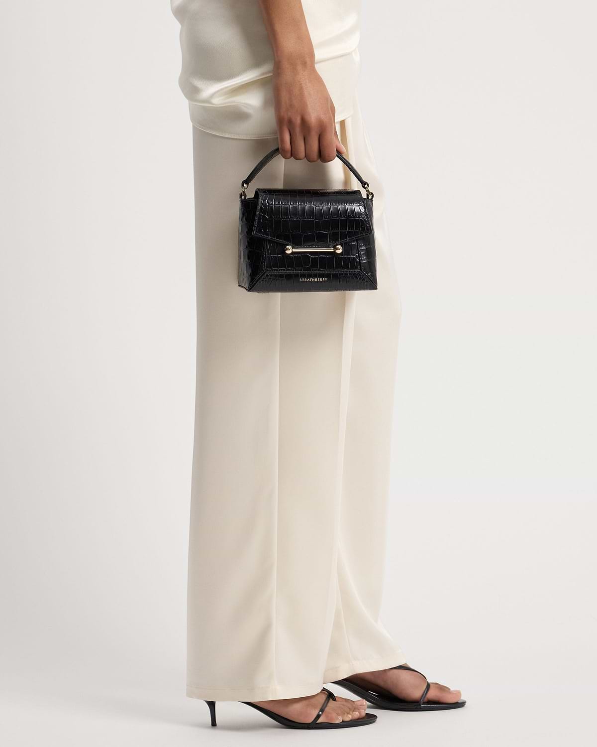 Hand holding Strathberry Mosaic Nano bag in soft croc with gold hardware.