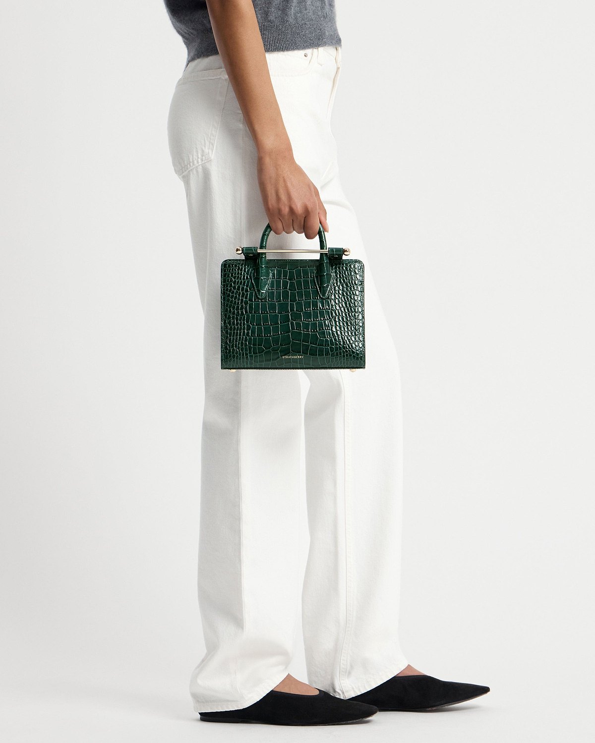 Hand holding green croc mini tote with gold bar handle and Strathberry logo.