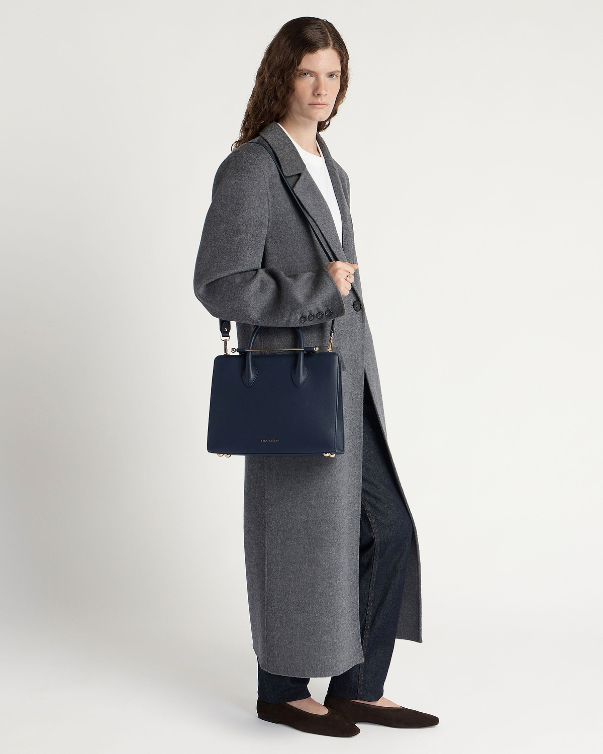 Model wearing long grey coat holding marine blue midi tote bag with strap.