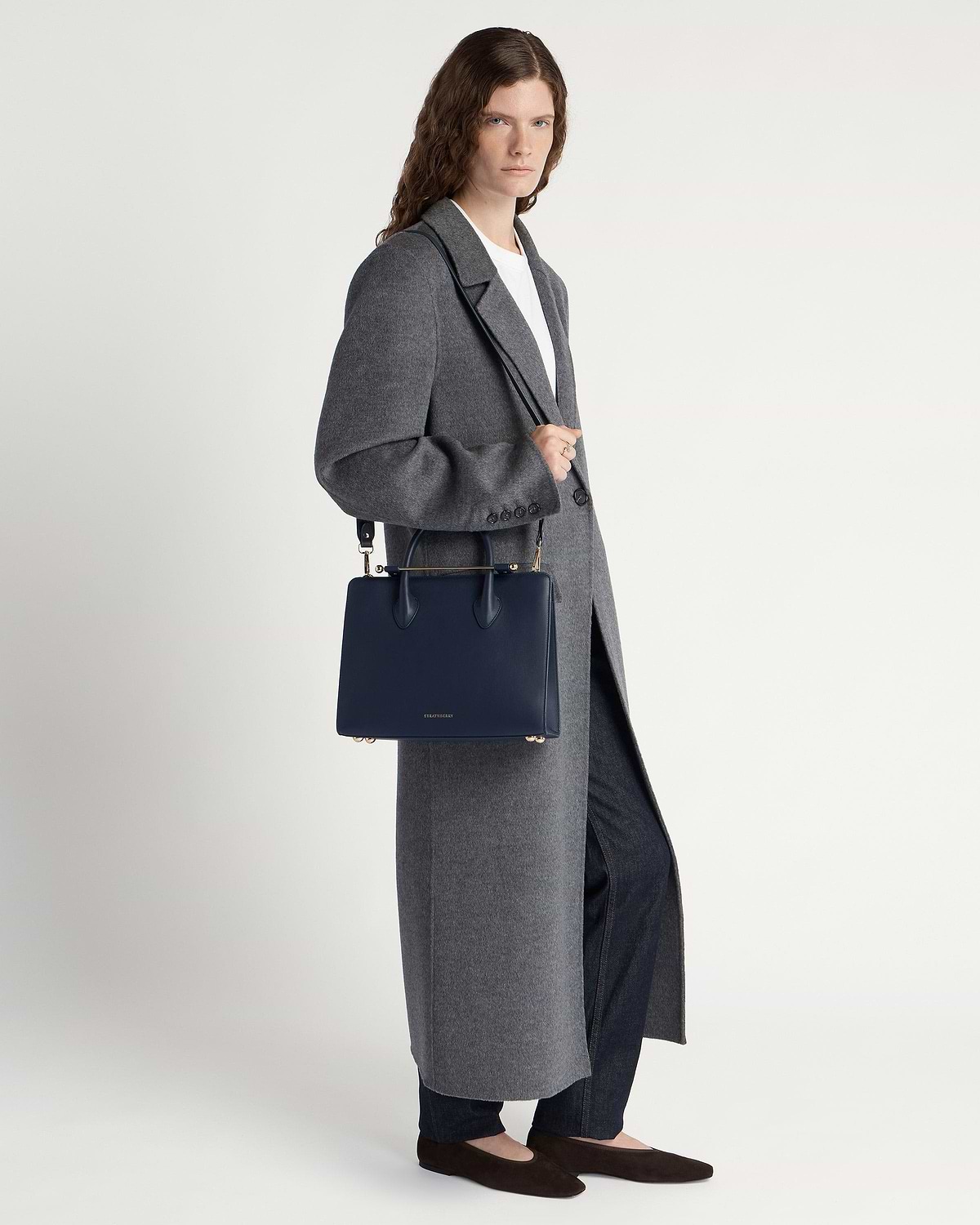 Model wearing long grey coat holding marine blue midi tote bag with strap.