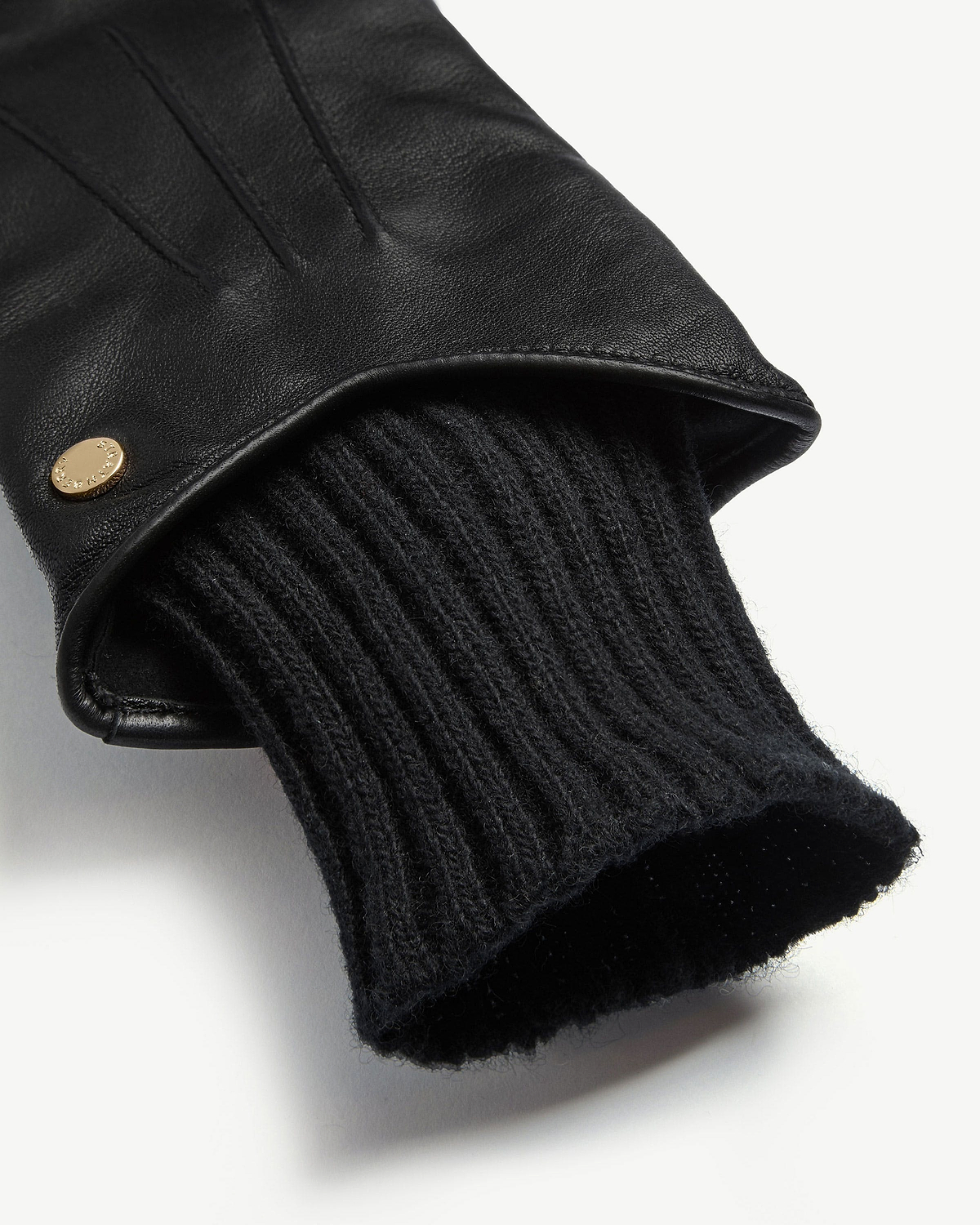 Close-up of black leather glove showing ribbed knit cuff and gold stud.