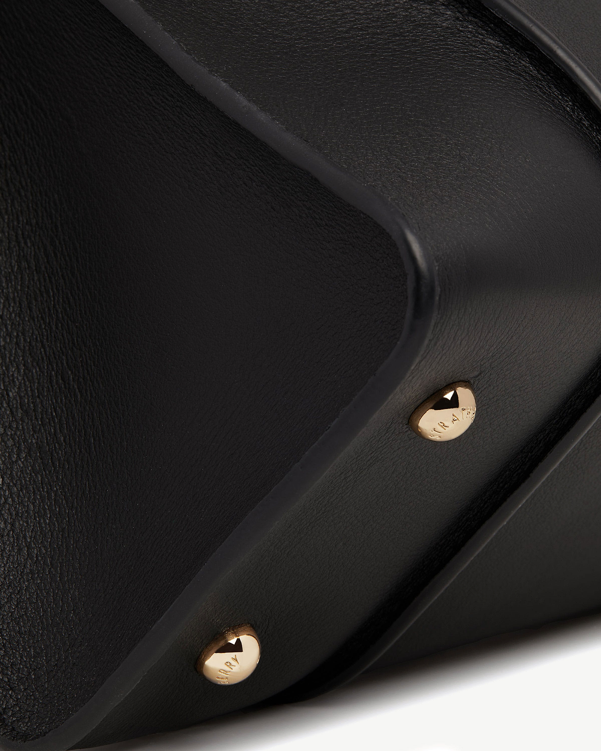 Close-up of black bag corner with gold studs and pebbled leather texture