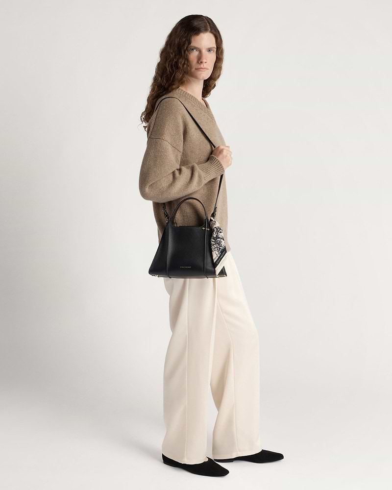 Woman wearing beige sweater and cream trousers carrying black Arkshell bag with patterned scarf.