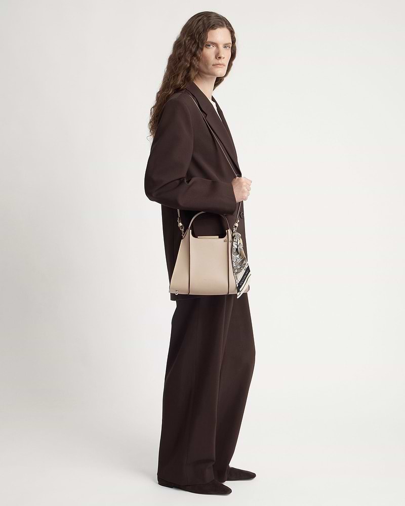 Model in brown suit holding an oat-coloured structured leather handbag with silk scarf.