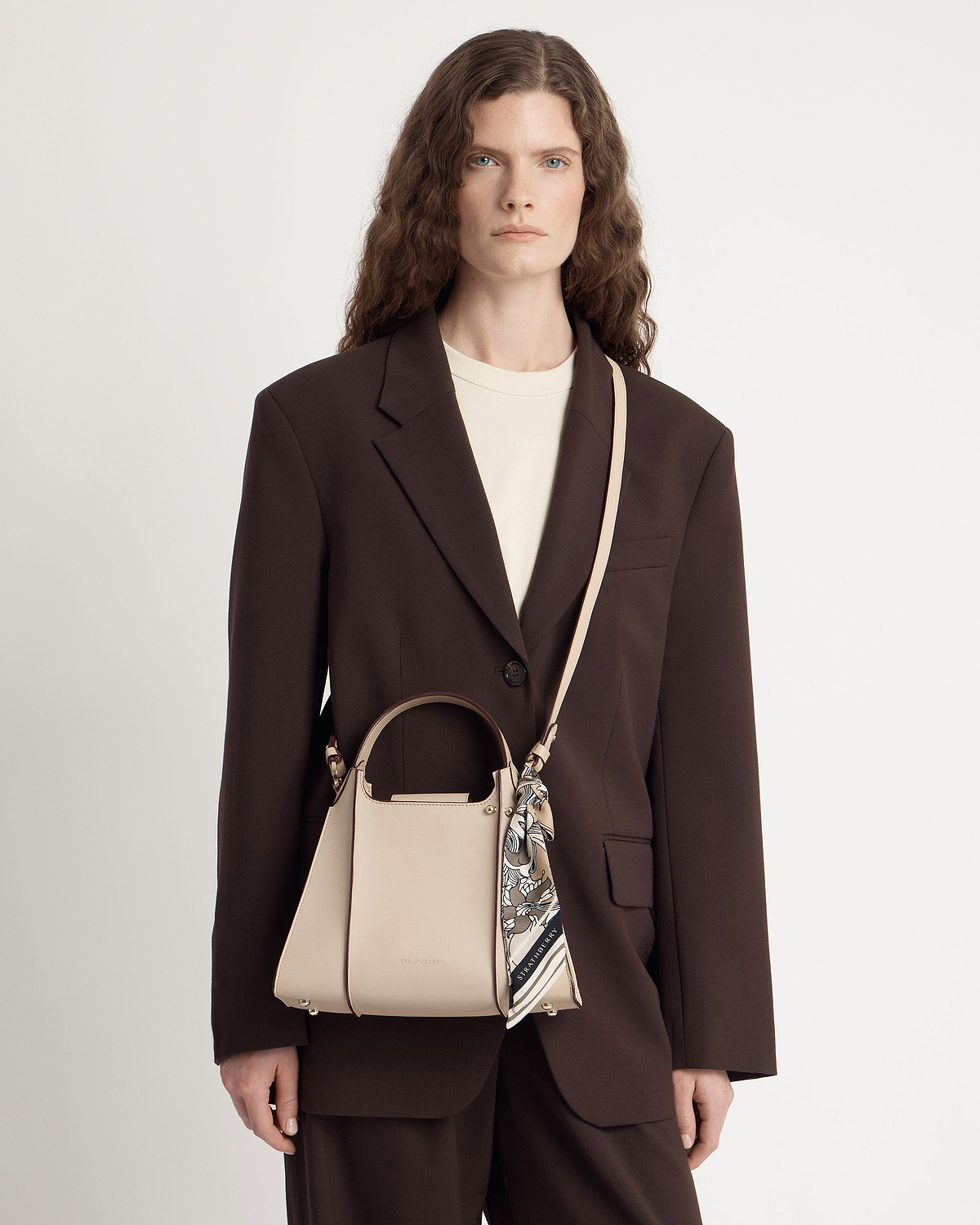 Model wearing oat Arkshell handbag with top handle, cross-body strap and tied scarf.