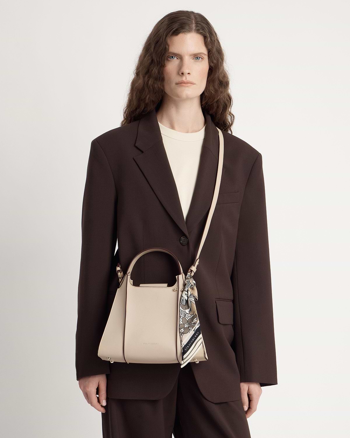 Model wearing oat Arkshell handbag with top handle, cross-body strap and tied scarf.