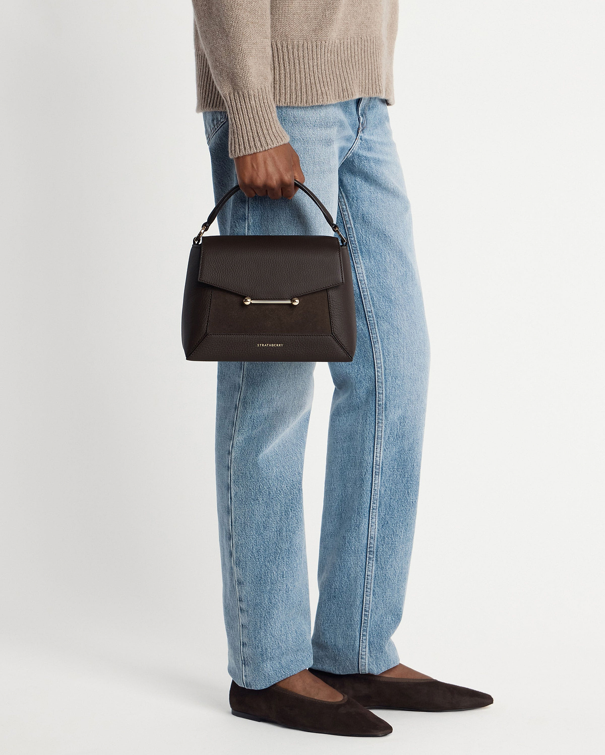 Model holding dark chocolate suede and leather mosaic bag by Strathberry.
