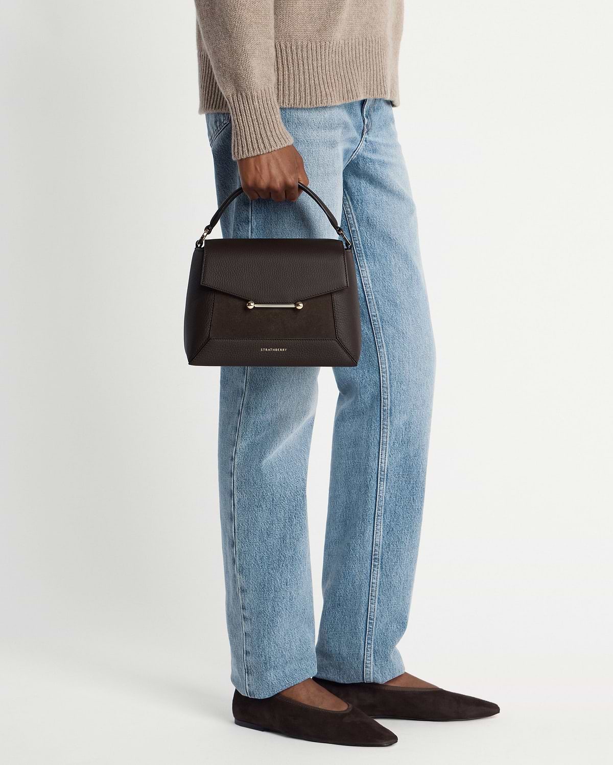 Model holding dark chocolate suede and leather mosaic bag by Strathberry.