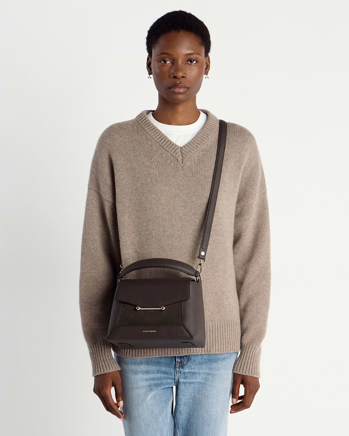 Model wearing dark chocolate mosaic bag by Strathberry with cross-body strap.