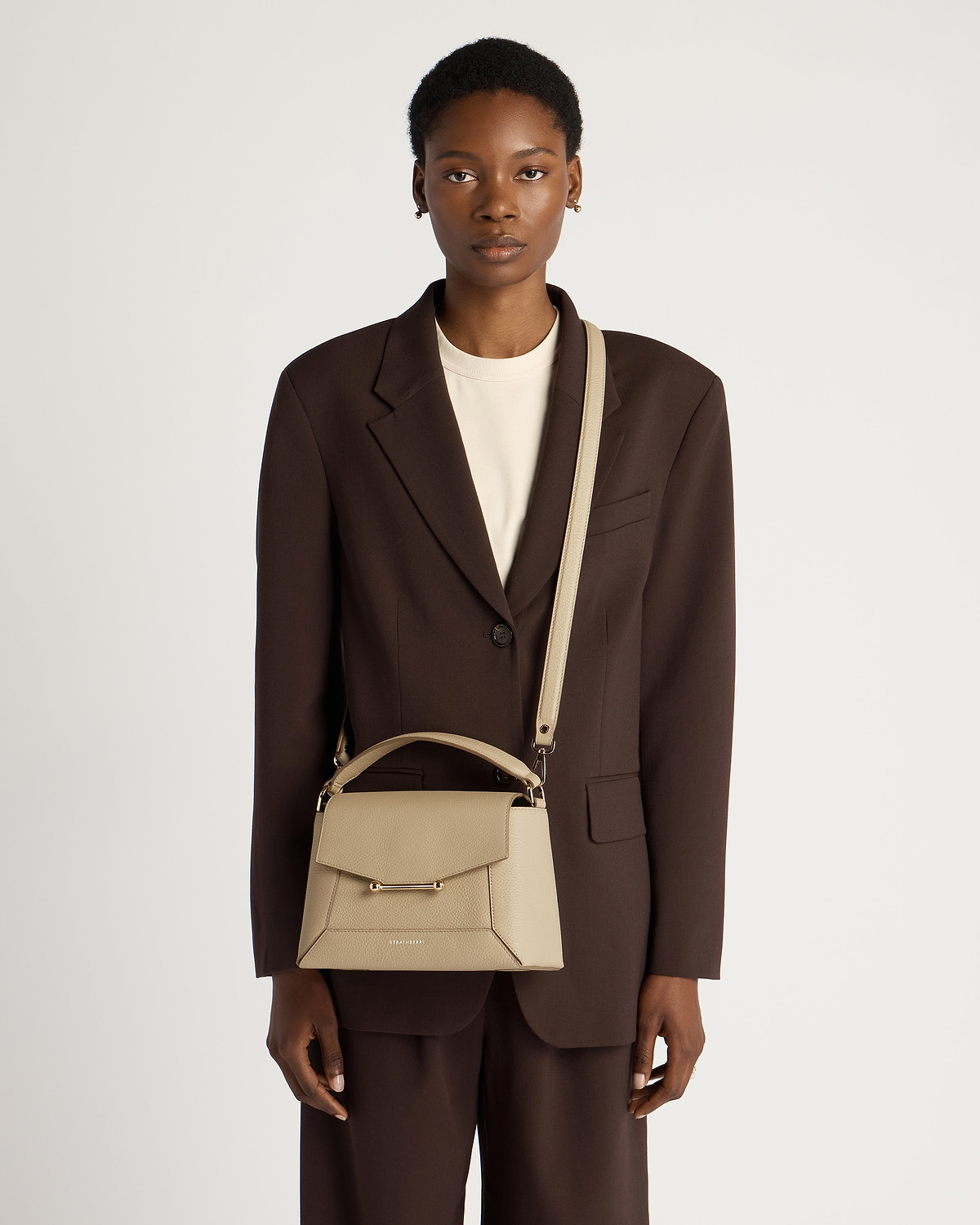 Model wearing brown blazer carrying sand mosaic bag by Strathberry with shoulder strap.