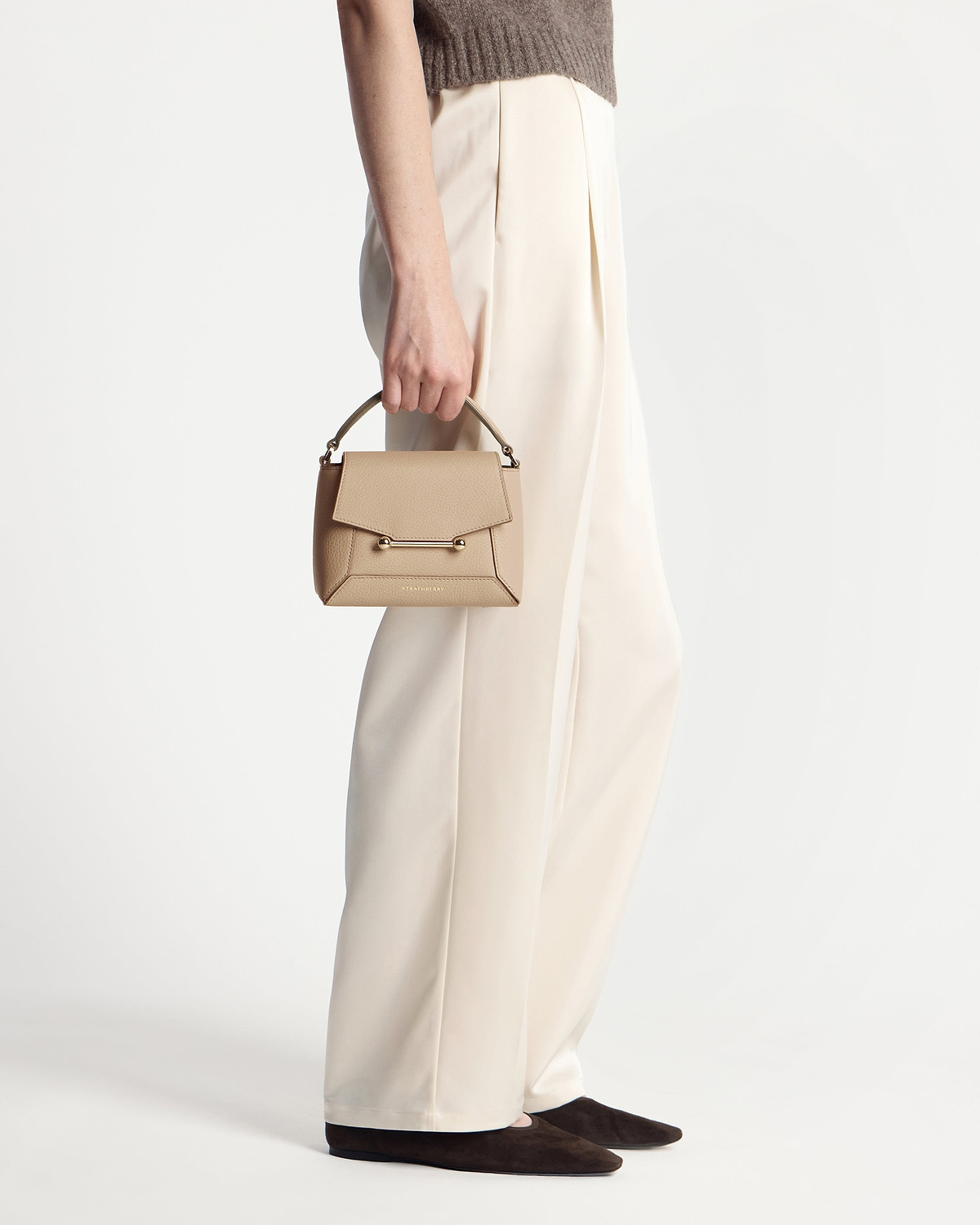 Model's waist and hand holding a Strathberry Mosaic Nano bag in sand.