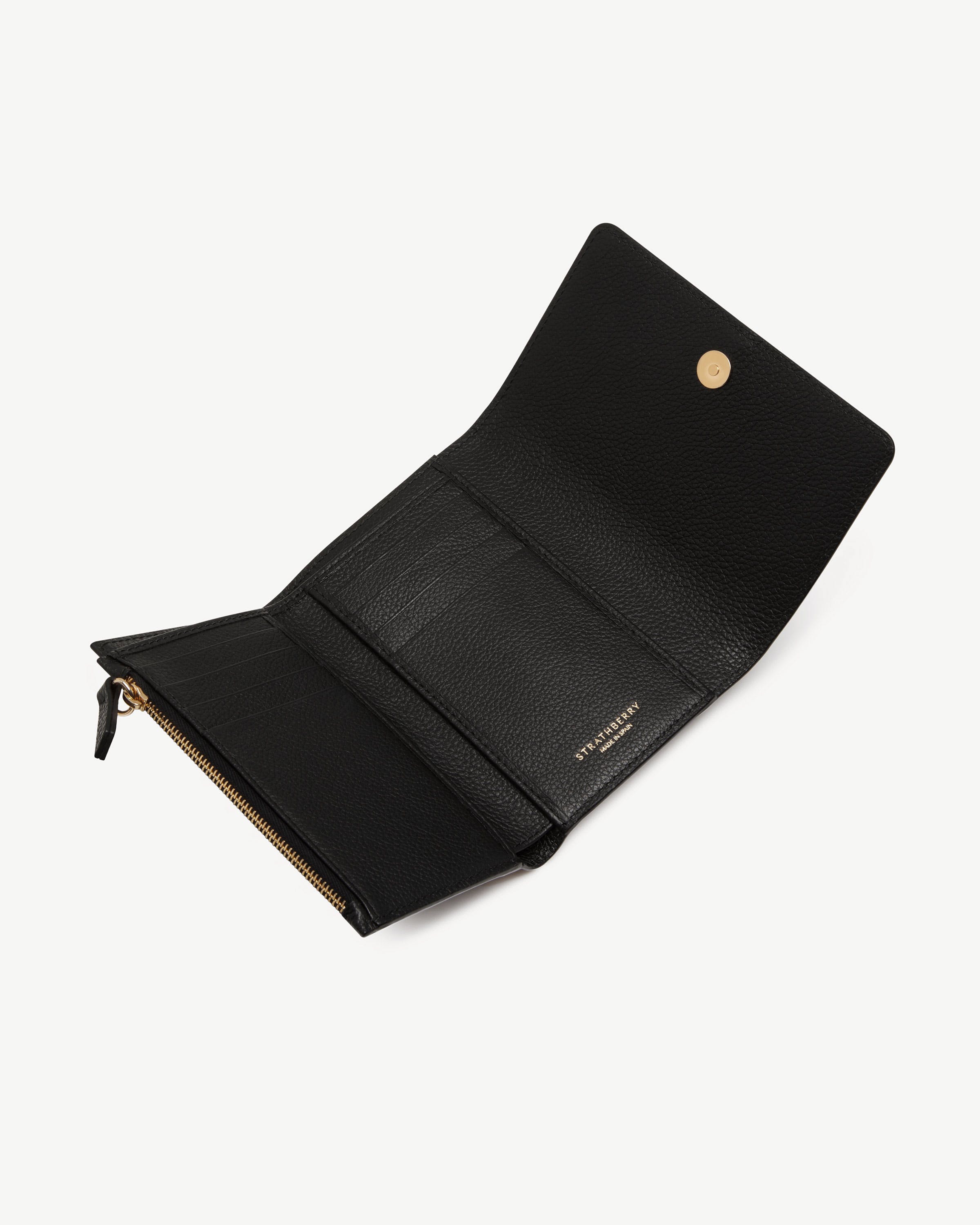 Black trifold wallet open showing card slots, zip coin pocket, gold Strathberry logo.