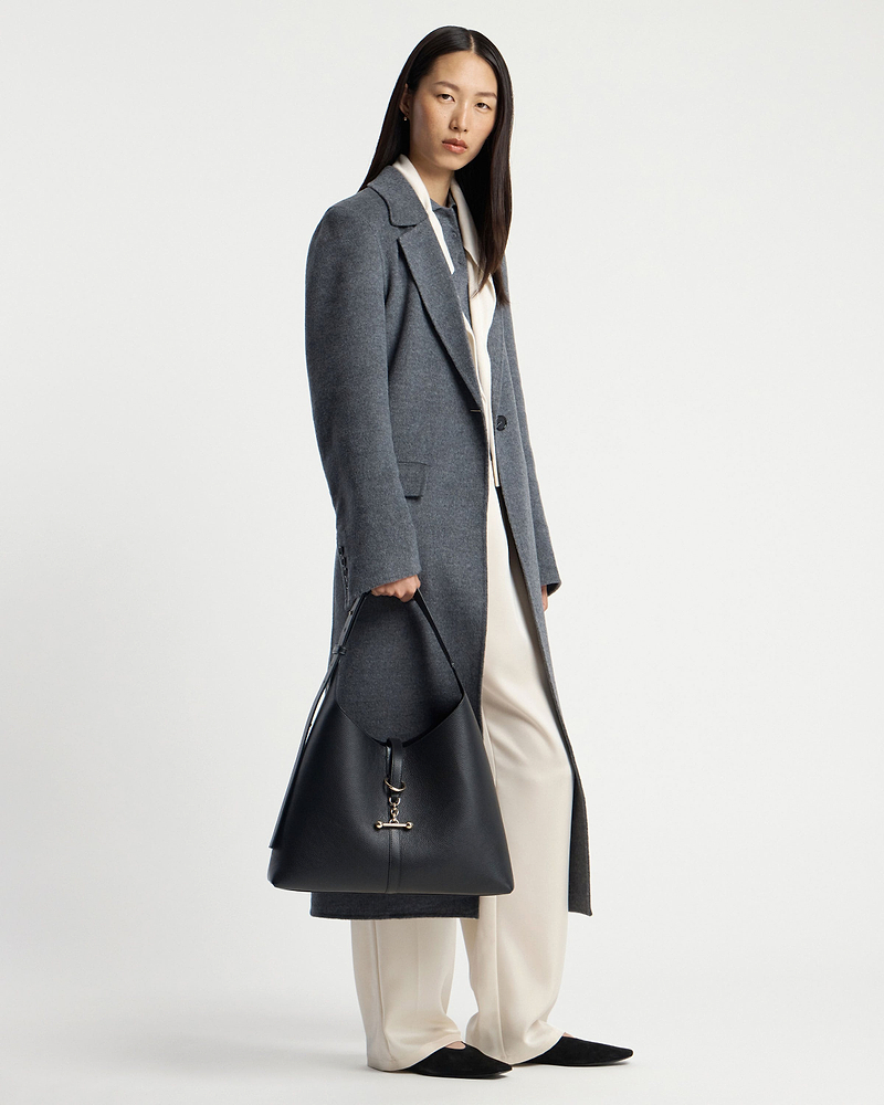 Model wearing grey coat holding black leather hobo bag with gold hardware.