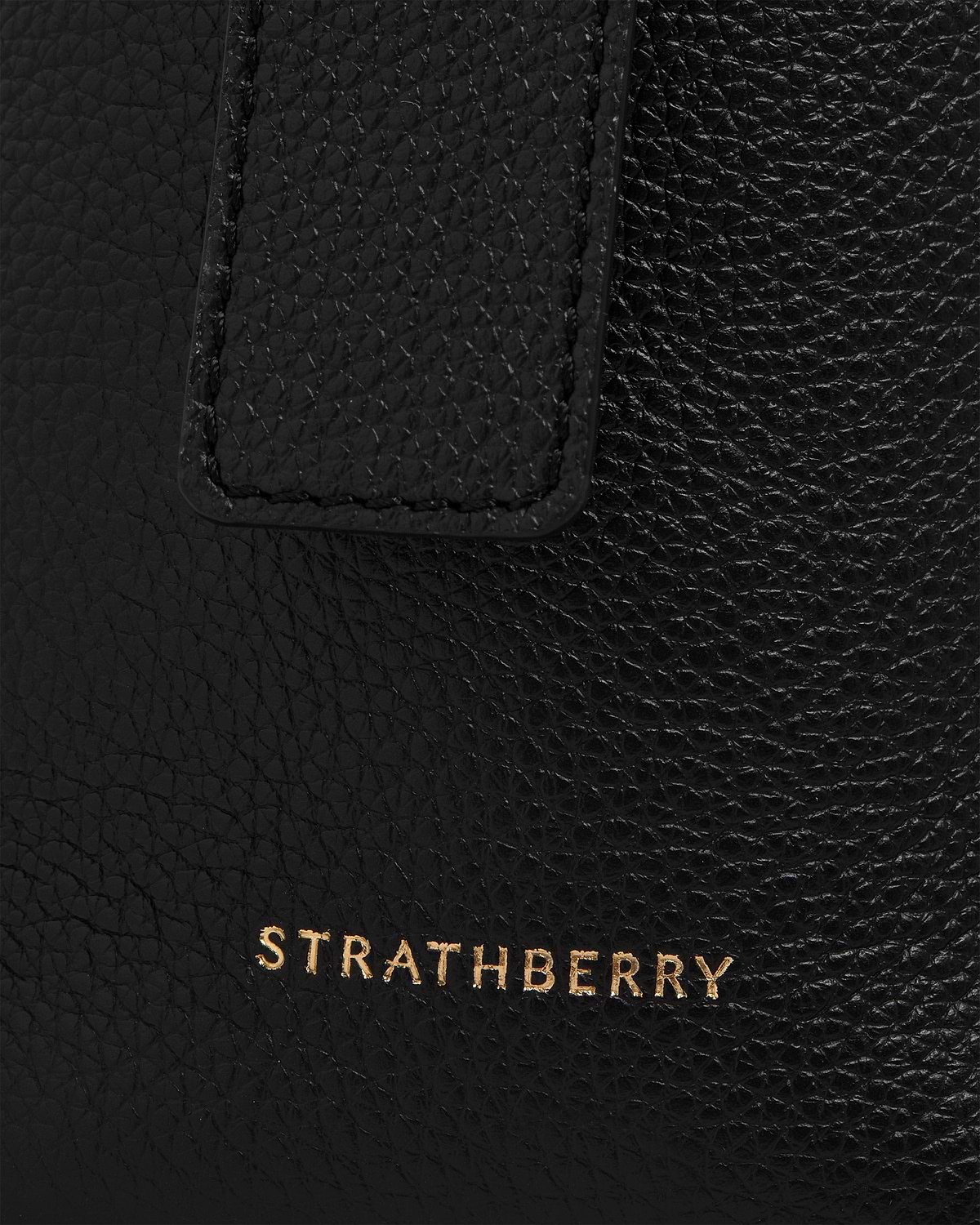 Black pebbled leather with stitched tab and gold Strathberry logo visible.