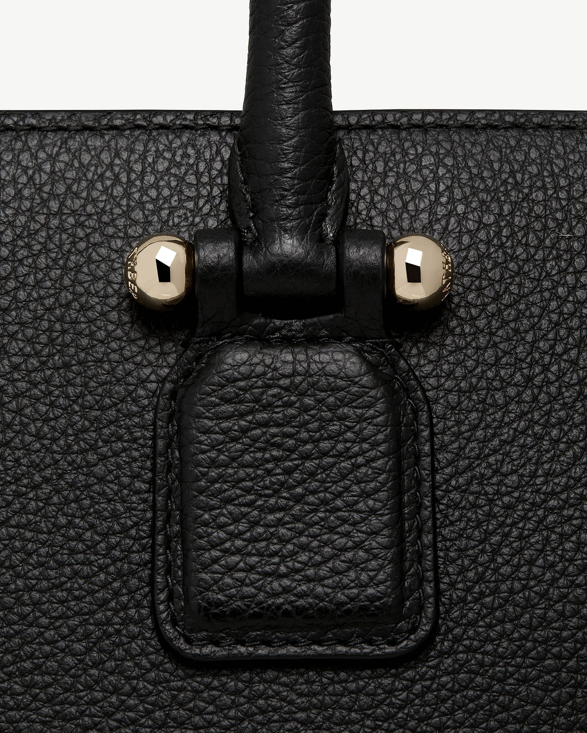 Close-up of black pebbled leather bag handle attachment with two gold studs.