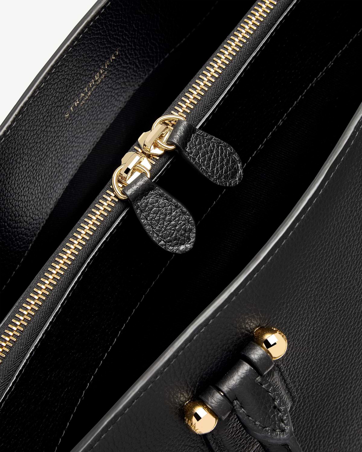 Close-up of black Strathberry bag interior showing gold zip and leather pull tabs.