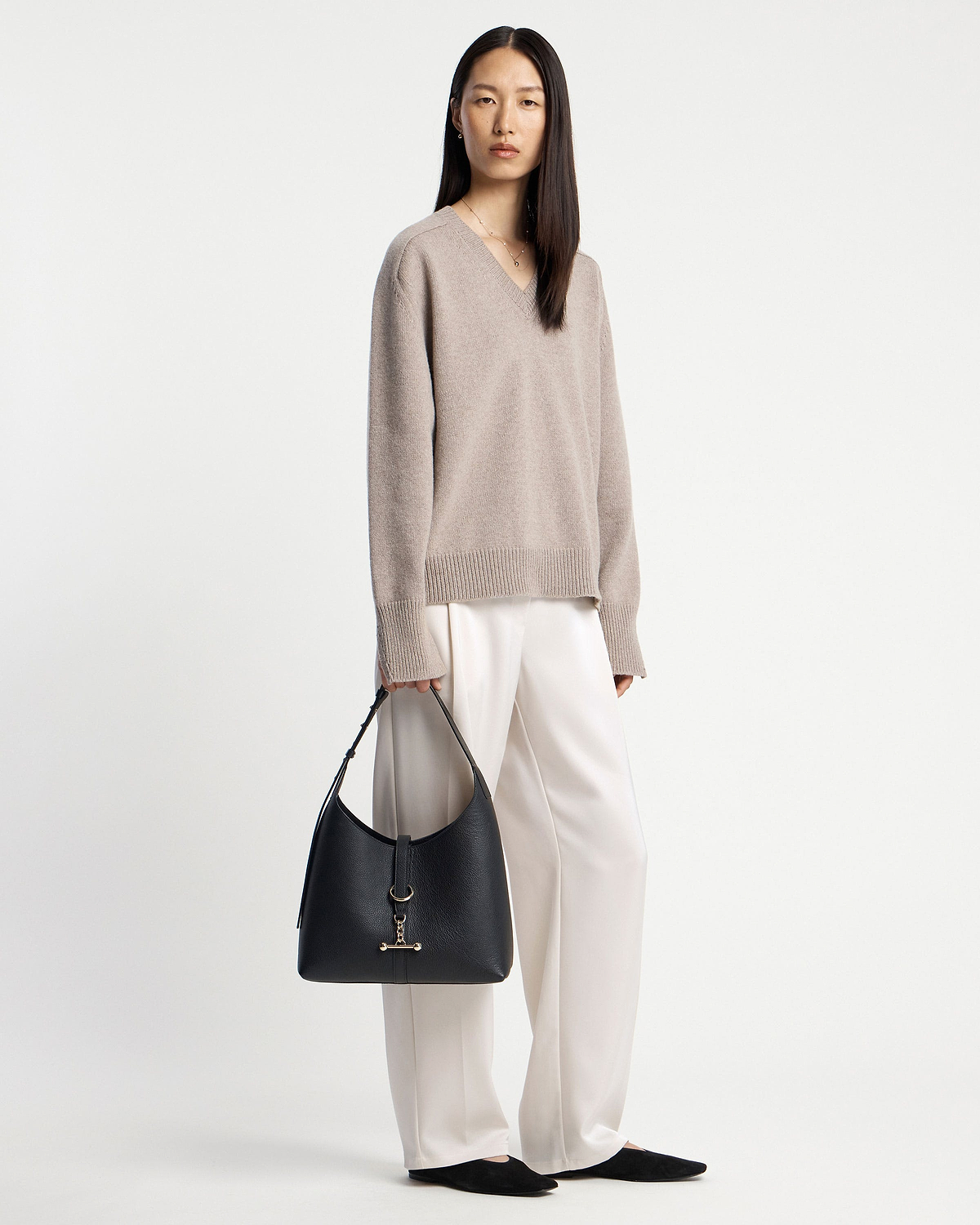 Woman in beige jumper holding a black hobo bag at her side.