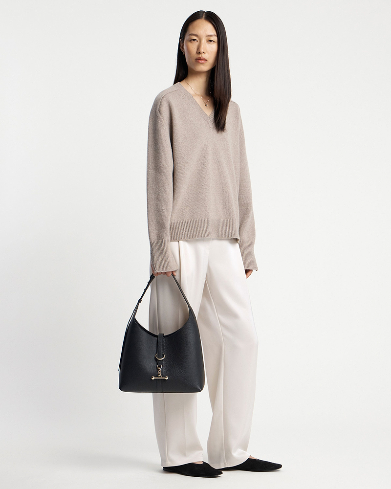 Woman in beige jumper holding a black hobo bag at her side.