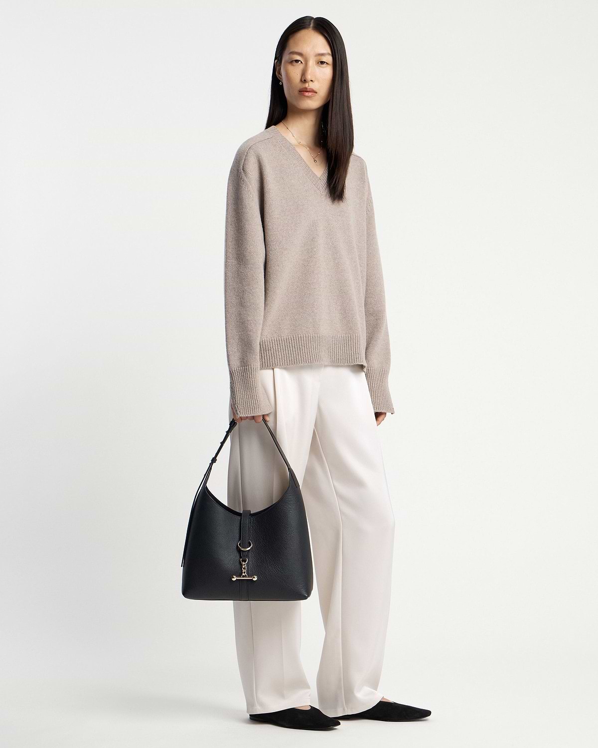 Woman in beige jumper holding a black hobo bag at her side.
