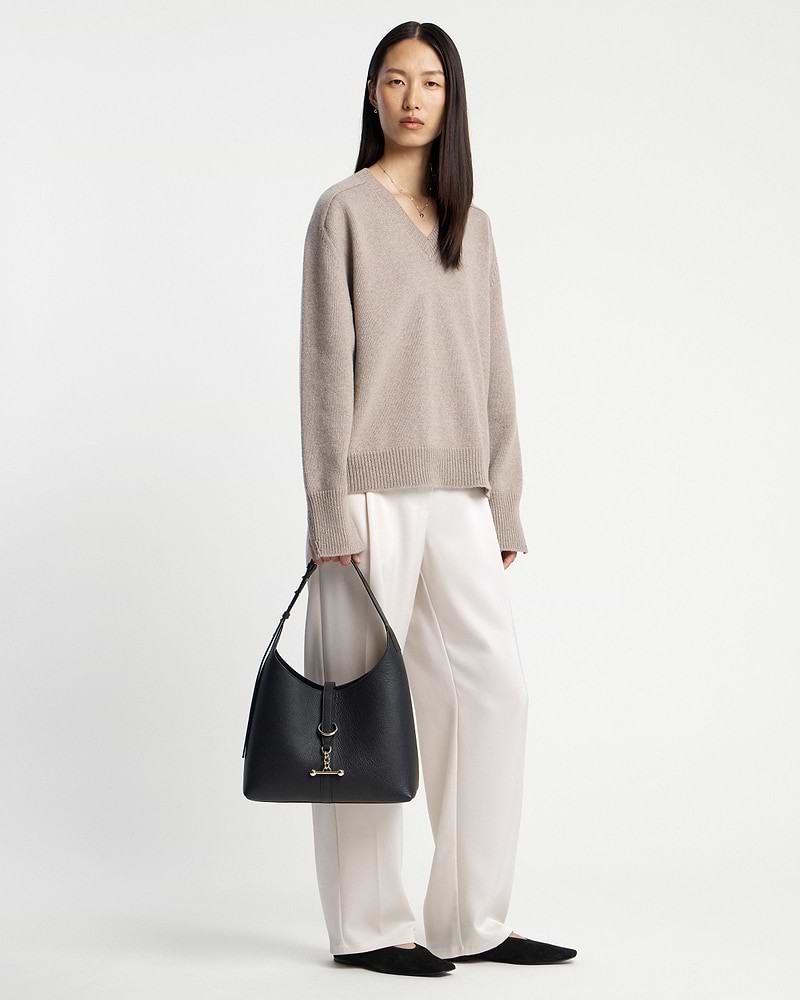 Woman in beige jumper holding a black hobo bag at her side.