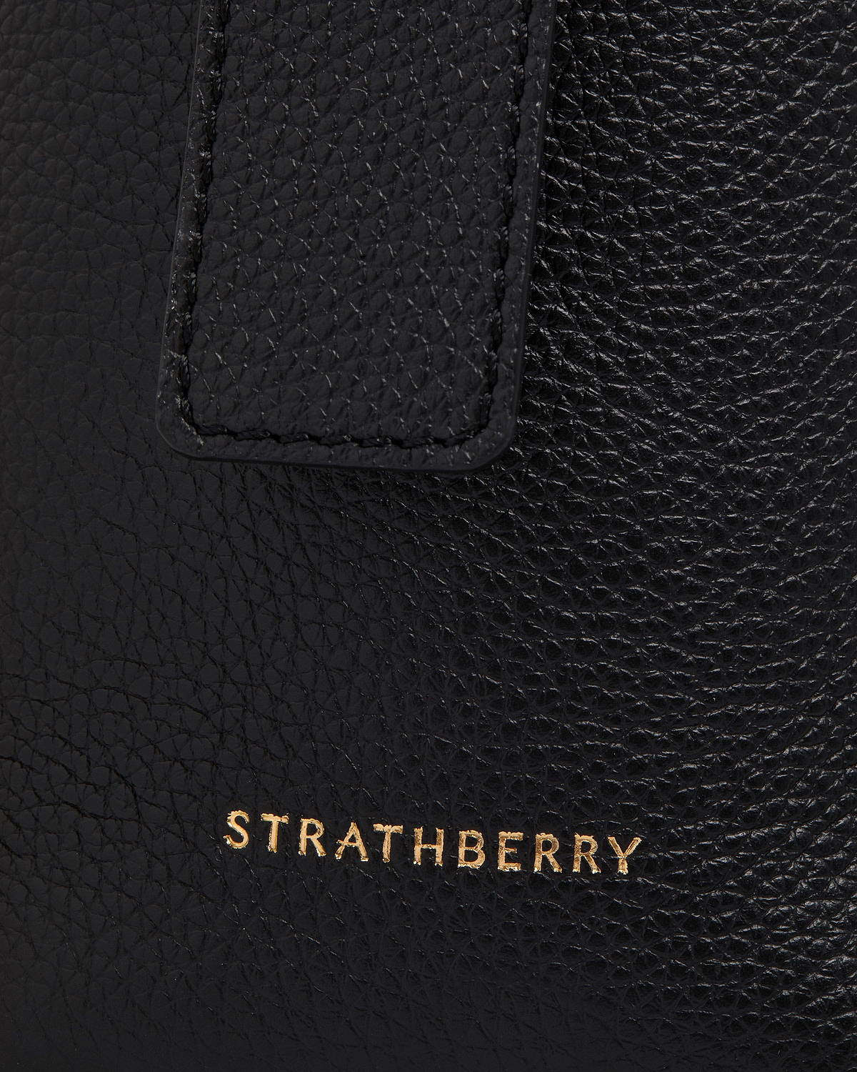 Black leather bag detail showing pebbled texture and gold Strathberry logo