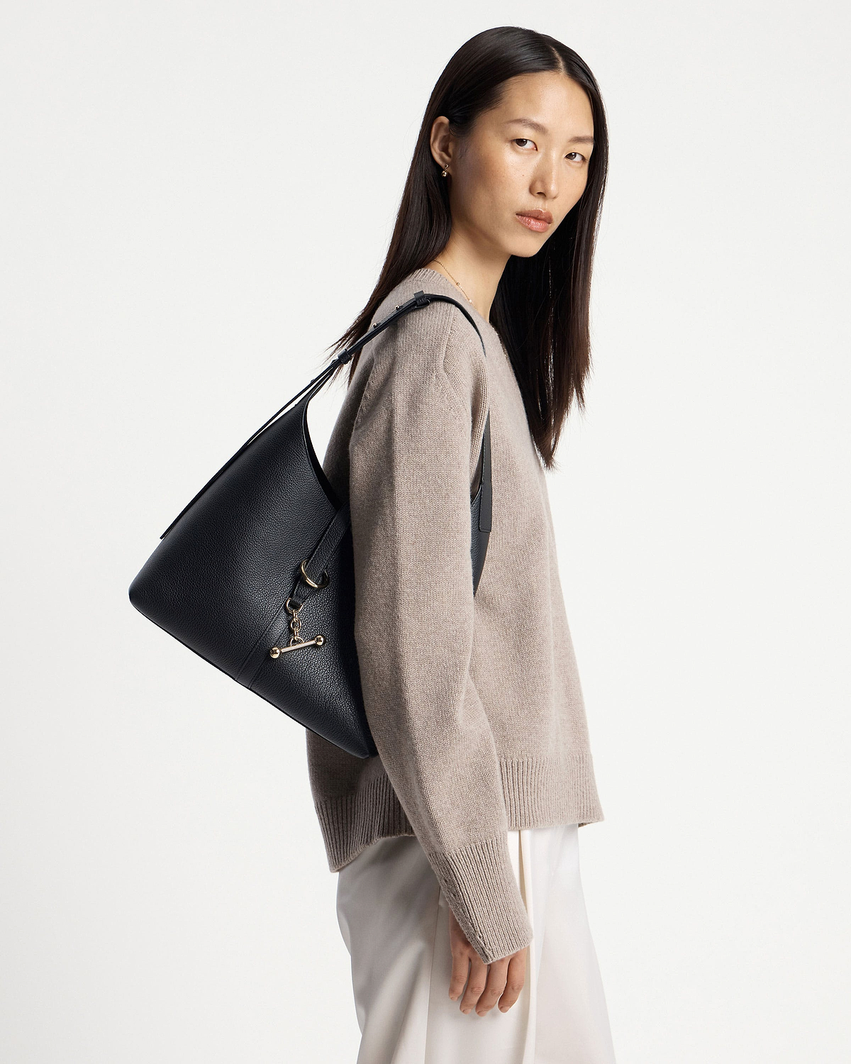 Model wearing a black Kite hobo bag on her shoulder, pebbled leather.