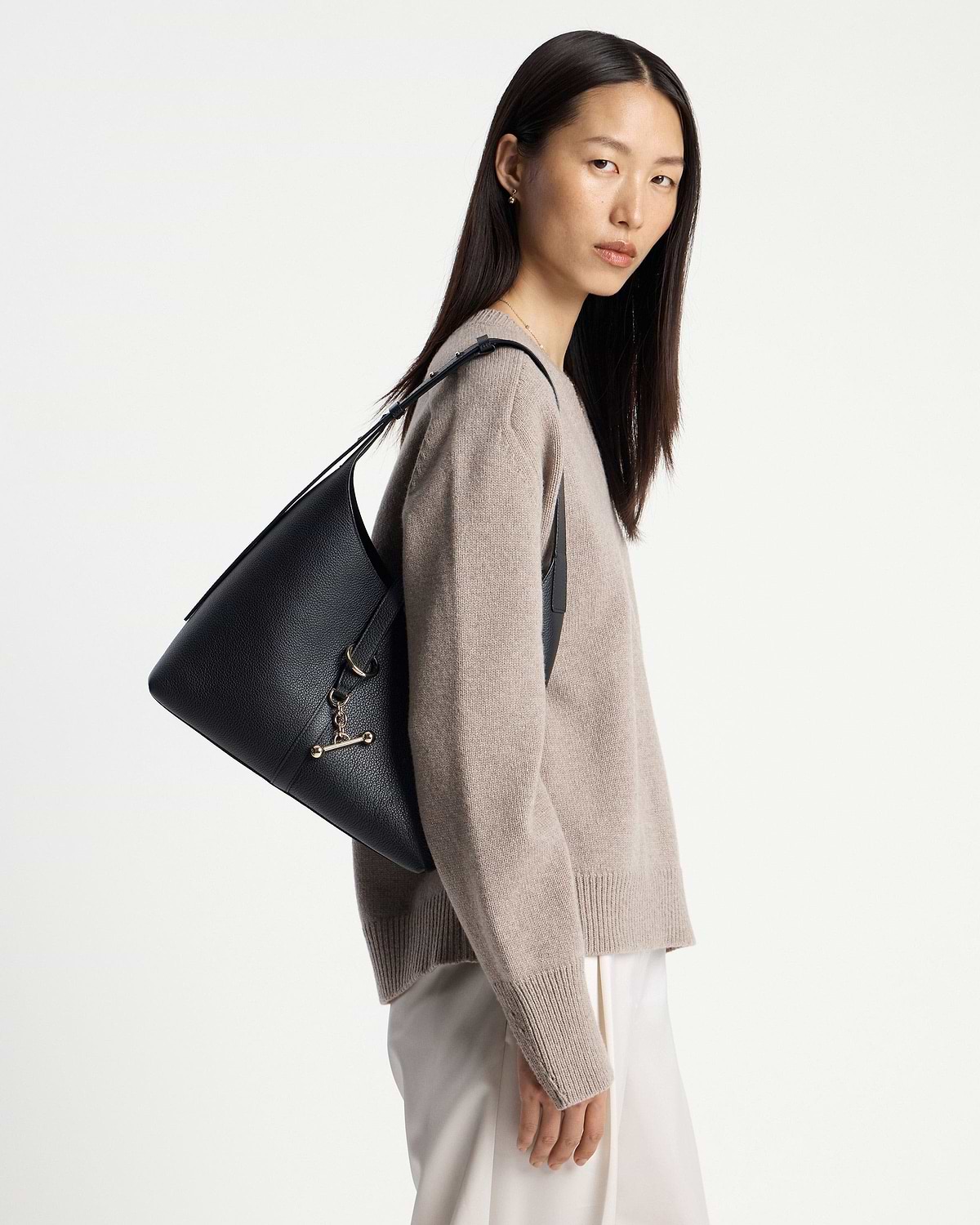 Model wearing a black Kite hobo bag on her shoulder, pebbled leather.
