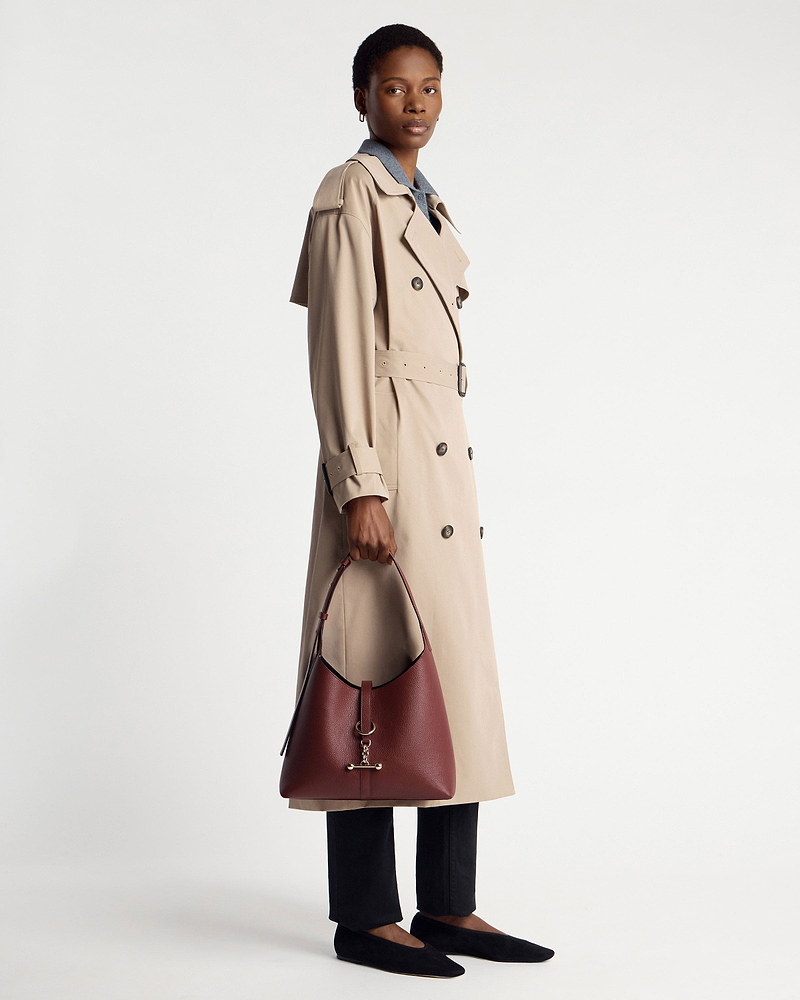Model holding oxblood Kite Hobo bag, wearing beige trench coat and black flats.