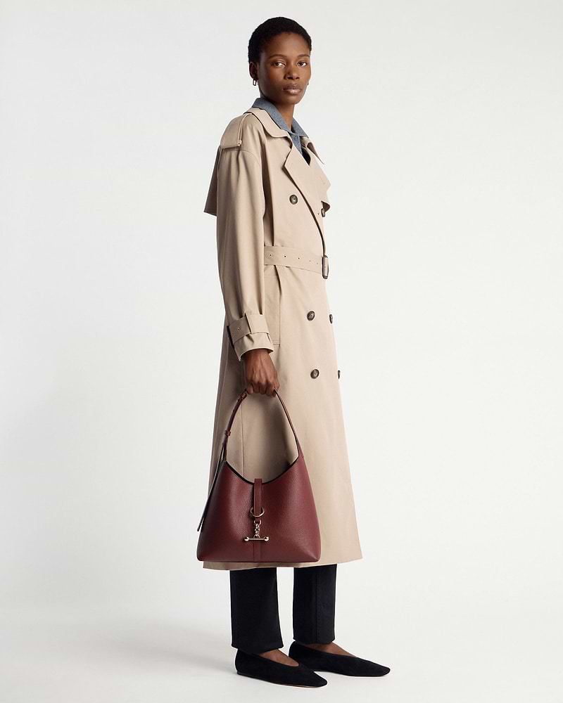 Model holding oxblood Kite Hobo bag, wearing beige trench coat and black flats.