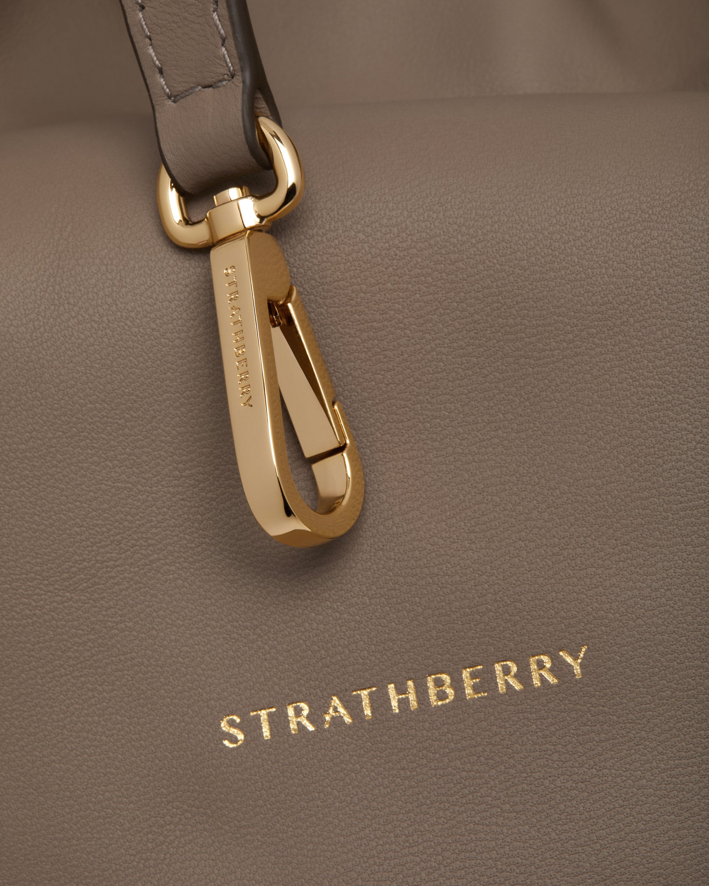 Taupe leather Charlotte Midi drawstring bag with engraved gold clasp and Strathberry logo.