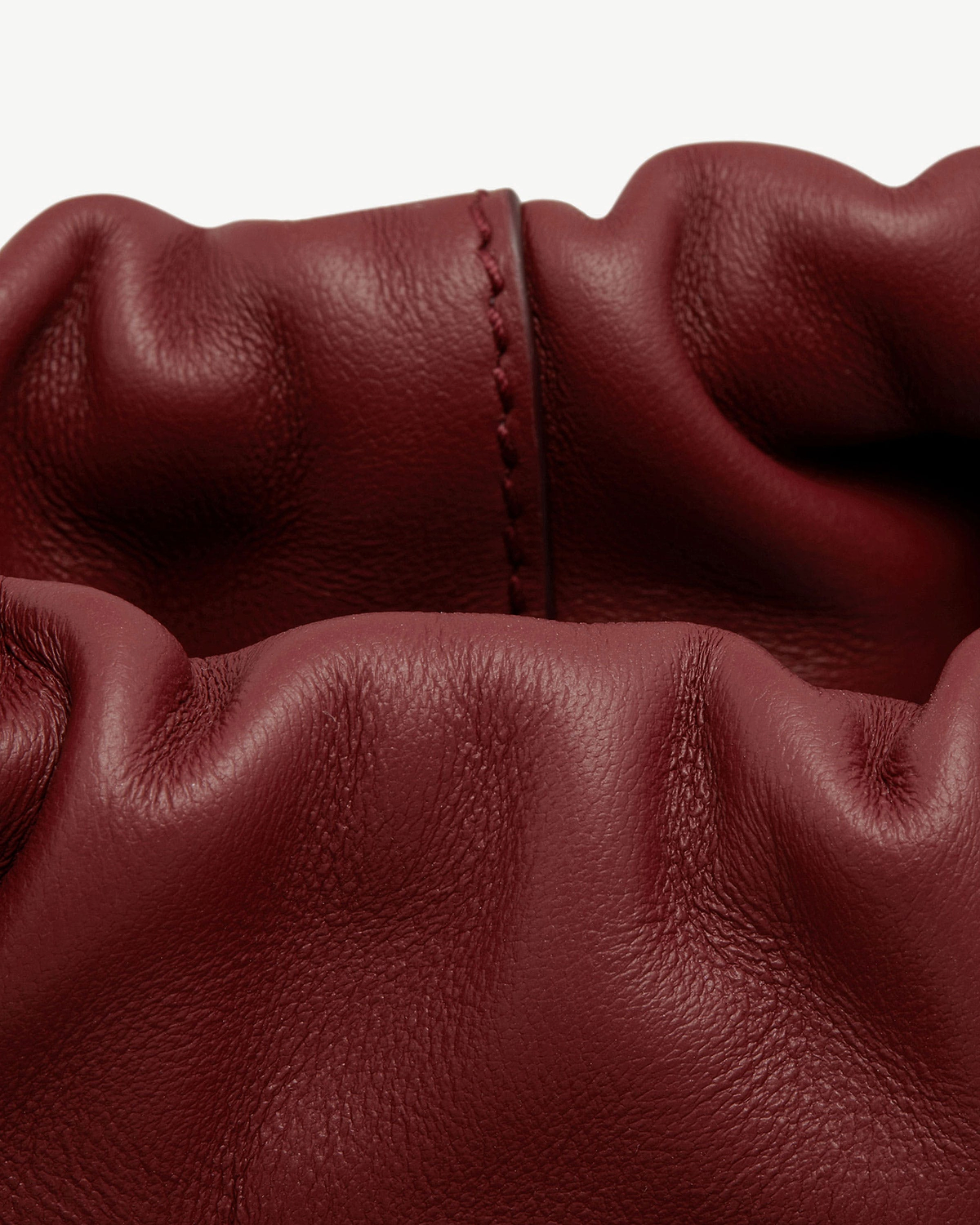 Oxblood leather drawstring bag with gathered top and visible central seam.