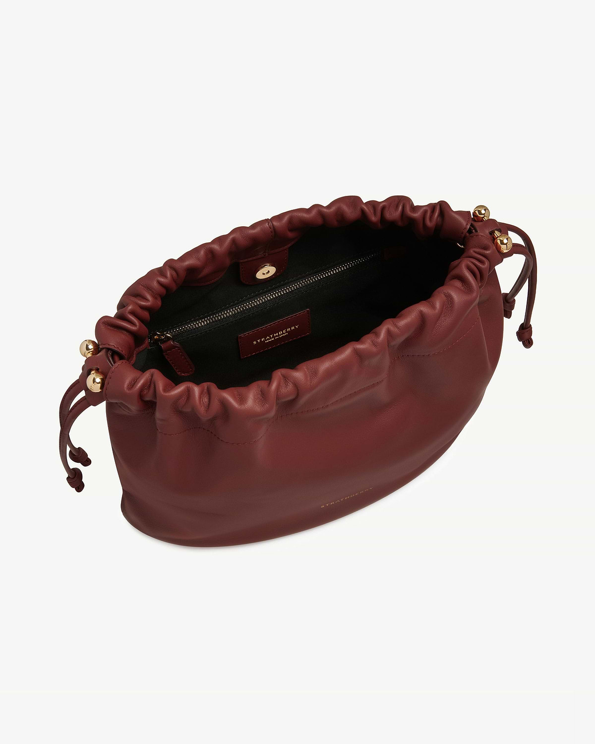 Strathberry oxblood Charlotte midi drawstring bag open, showing interior zip pocket and gold hardware.
