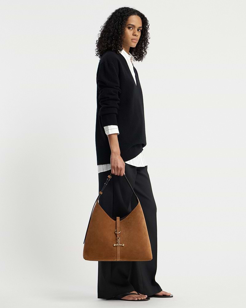 Model holding tan suede hobo bag with gold hardware, wearing black jumper.