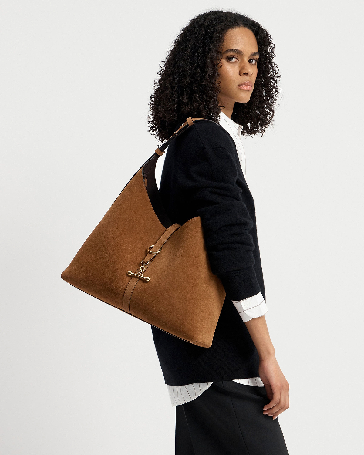 Woman wearing black jumper and white shirt carrying tan suede hobo shoulder bag.