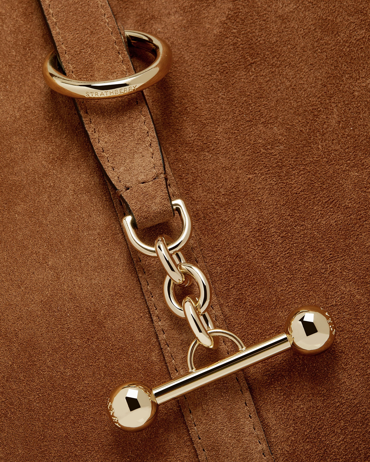 Tan suede detail showing Strathberry engraved gold ring, chain and toggle hardware.
