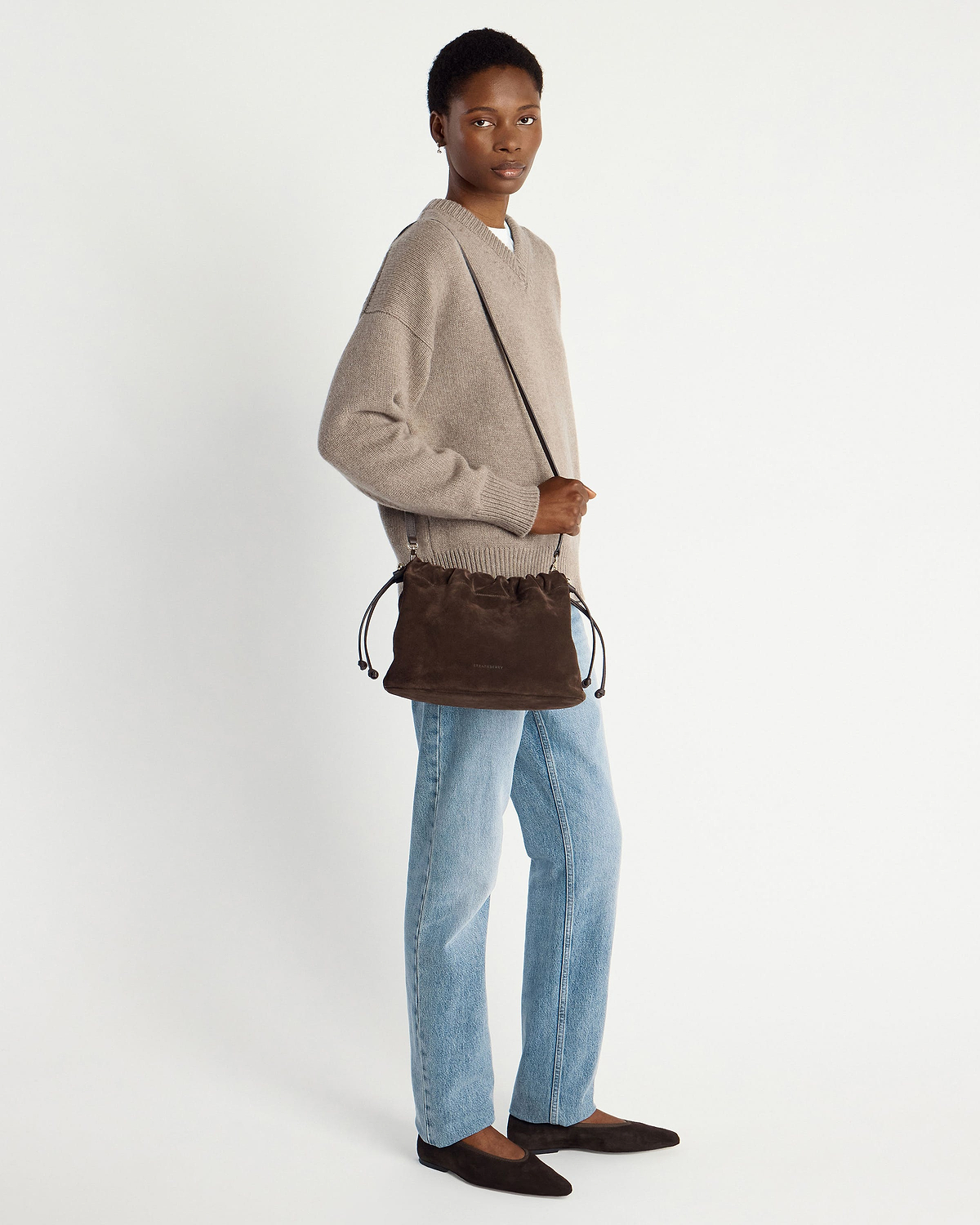 Model wearing chocolate suede drawstring bag crossbody, beige jumper and light jeans.
