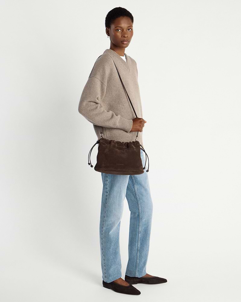 Model wearing chocolate suede drawstring bag crossbody, beige jumper and light jeans.