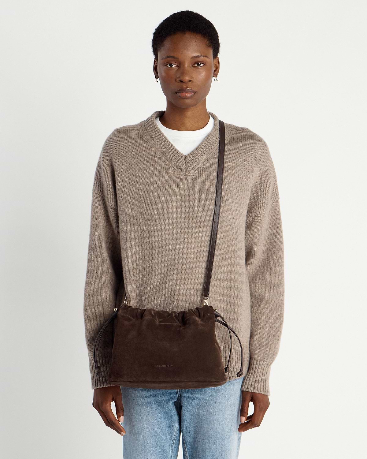 Woman wearing chocolate suede Charlotte Midi drawstring crossbody bag over knitted jumper
