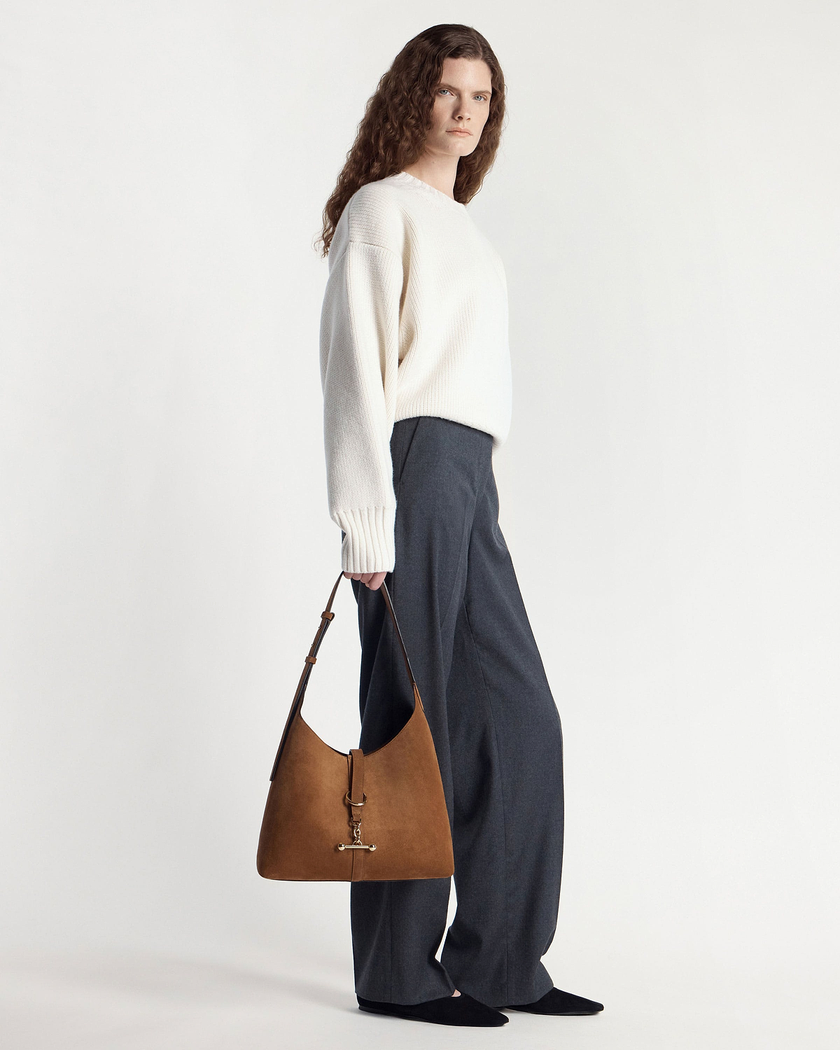 Model holding tan suede hobo bag with gold hardware at her side.