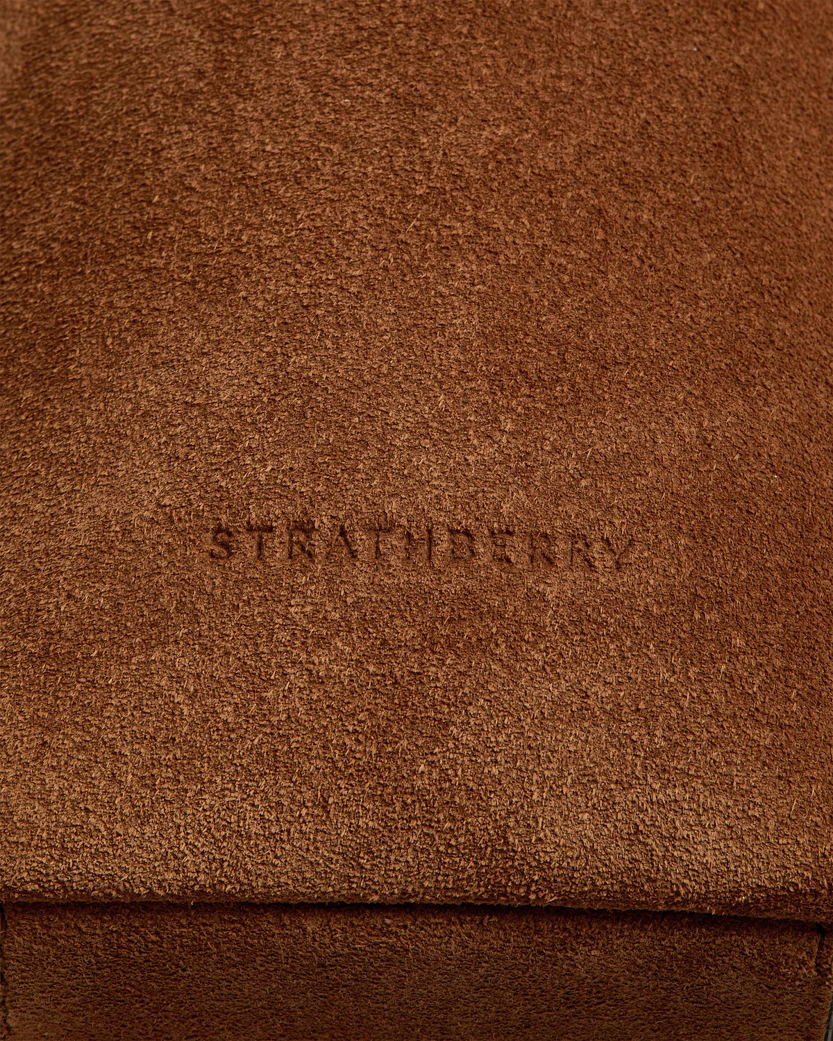 Tan suede bag flap with textured nap and faint embossed wordmark