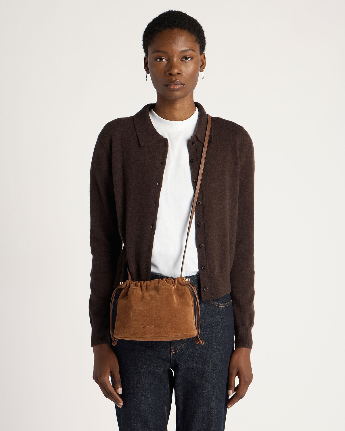Model wearing tan suede drawstring bag crossbody over brown cardigan and jeans.