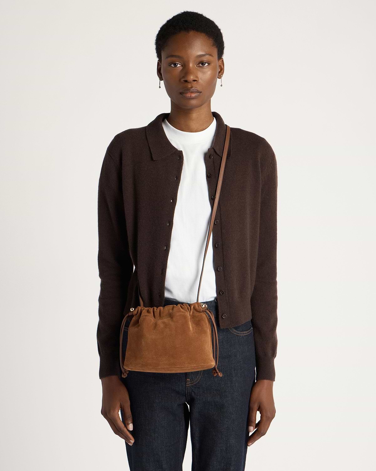 Model wearing tan suede drawstring bag crossbody over brown cardigan and jeans.