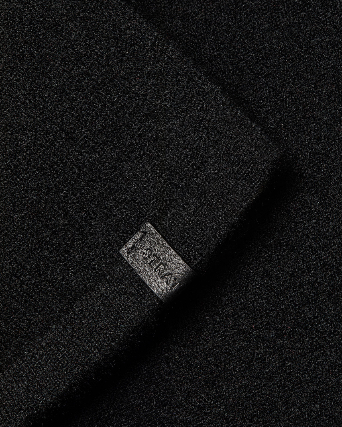 Black cashmere travel wrap with small Strathberry embossed leather tag visible.