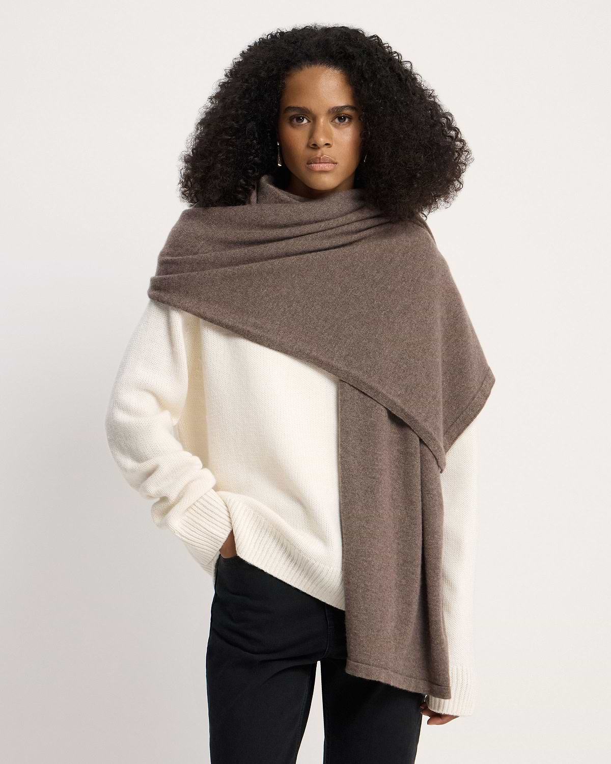 Model wearing otter-coloured cashmere travel wrap draped over cream jumper.