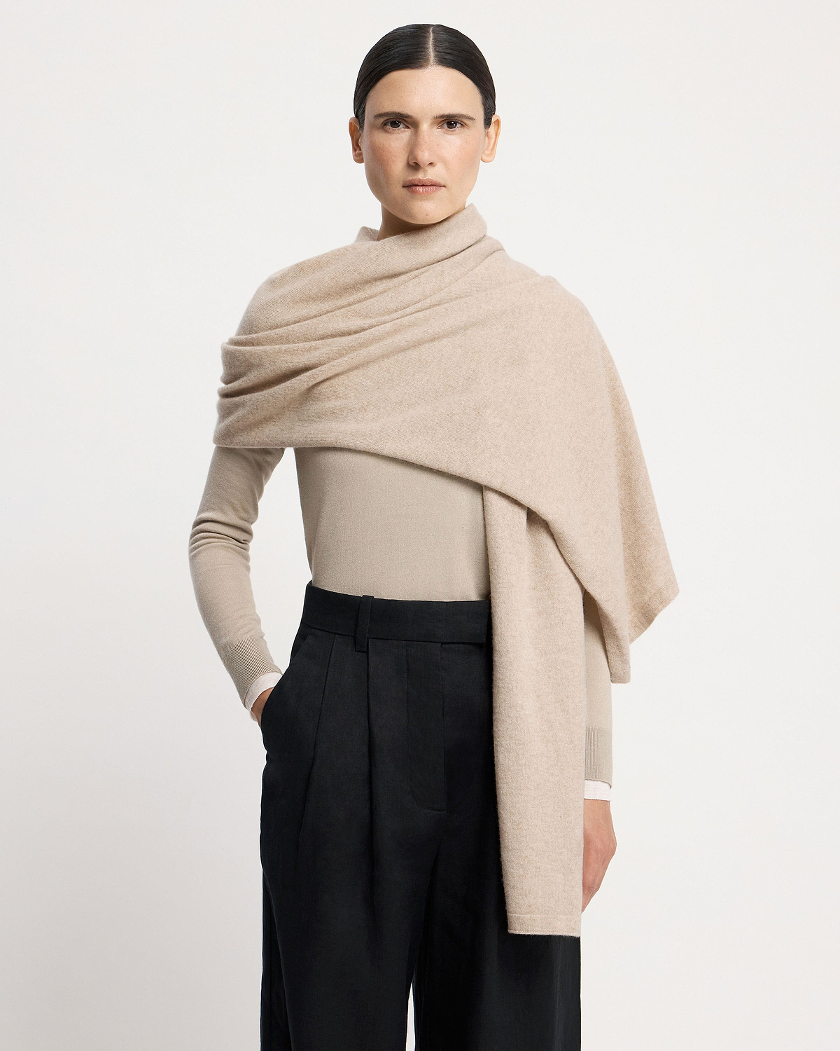 Model wearing an oat-coloured cashmere travel wrap draped over shoulders.