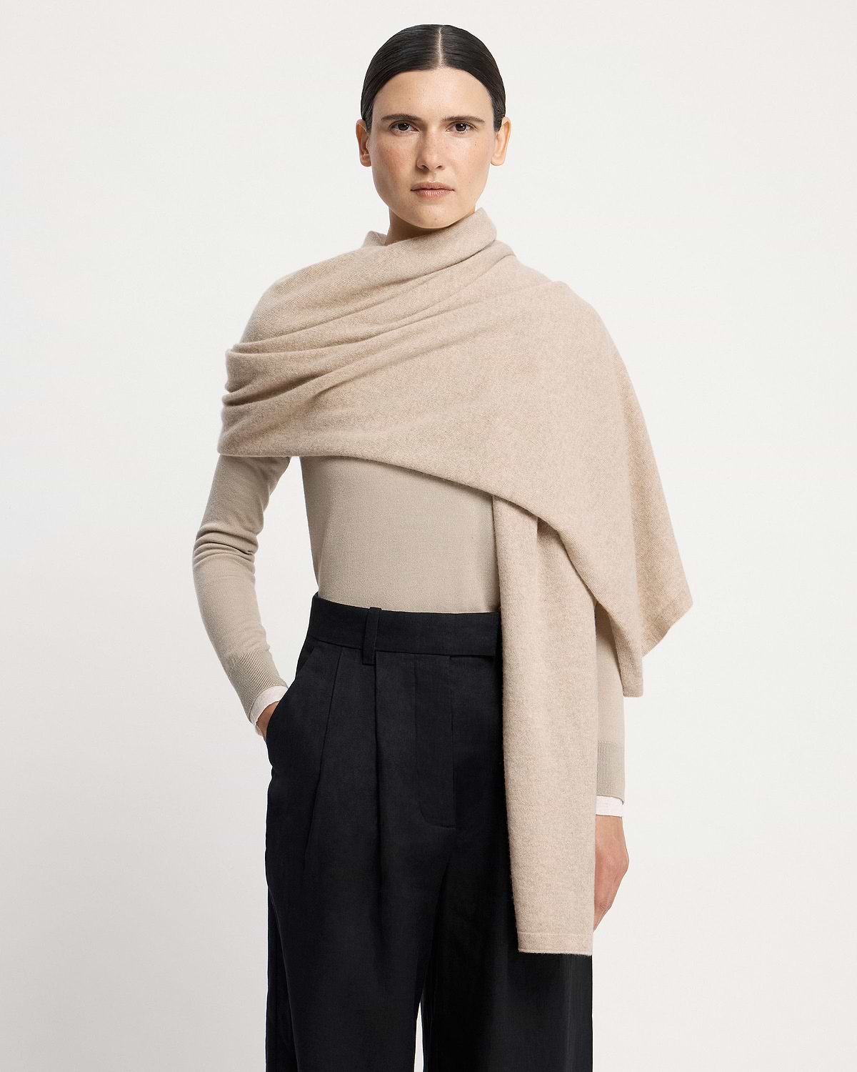 Model wearing an oat-coloured cashmere travel wrap draped over shoulders.