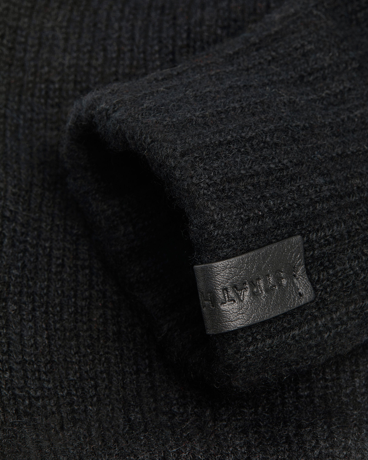 Black ribbed fingerless glove showing textured knit and leather tag